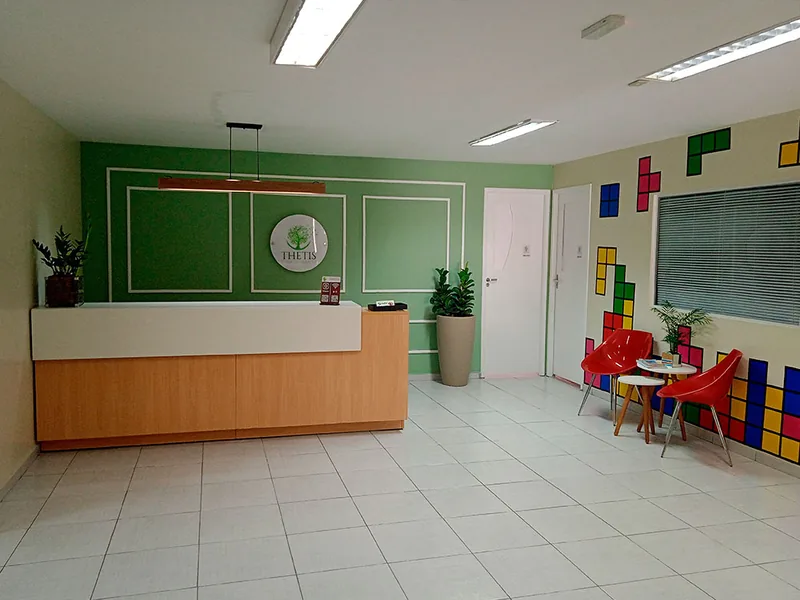 Recepção da clínica, com balcão de madeira e parede verde com o logotipo da Thetis