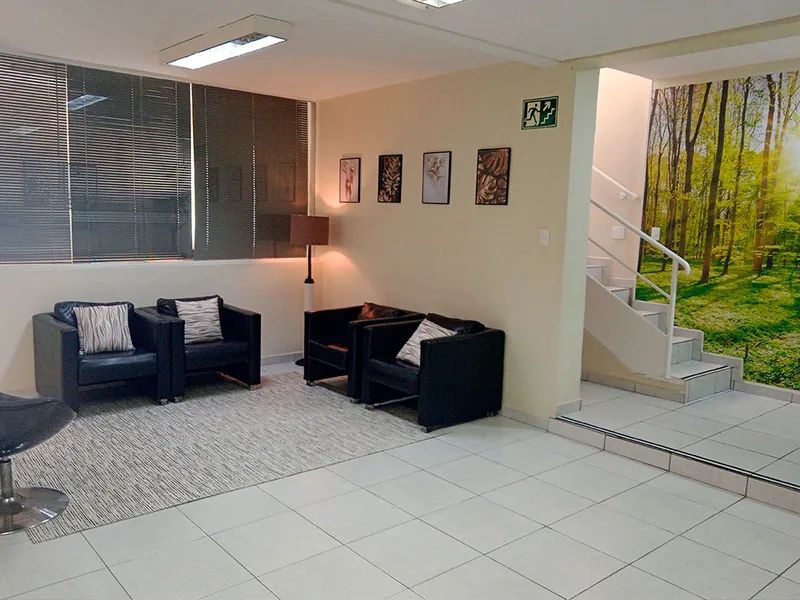 Sala de espera da clínica, com poltronas, tapete e um painel de floresta na parede